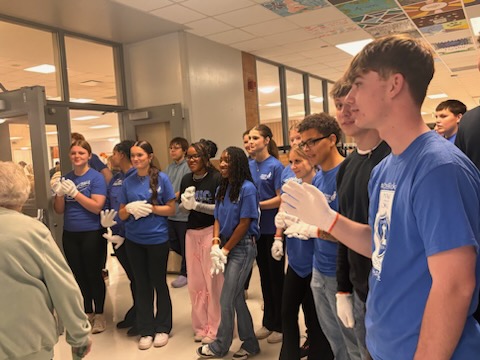 Student volunteers greet a guest entering the cafeteria for lunch.